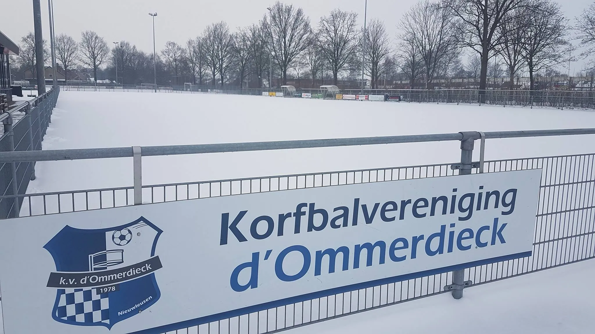 Het besneeuwde korfbalveld van d'Ommerdieck met het clubbord aan het hek.
